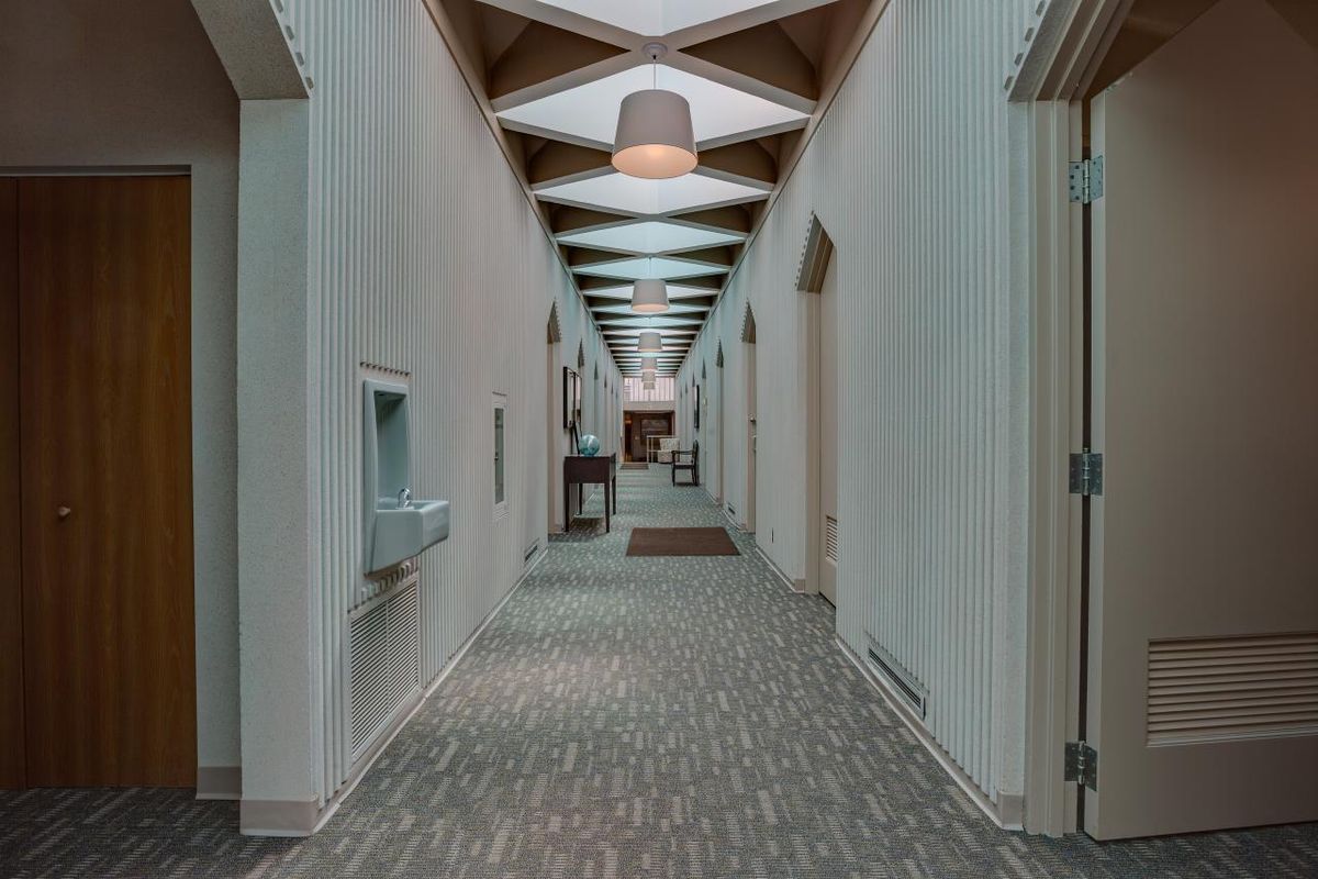 A hallway with carpeted floors and natural blue light coming from repeating square skylights.