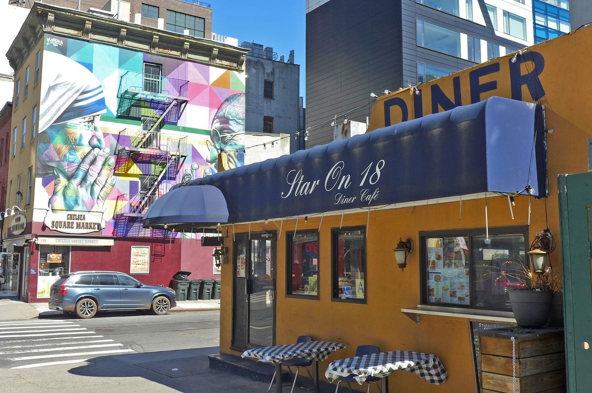 A diner with a blue awning, and mural of Mother Teresa in the background.