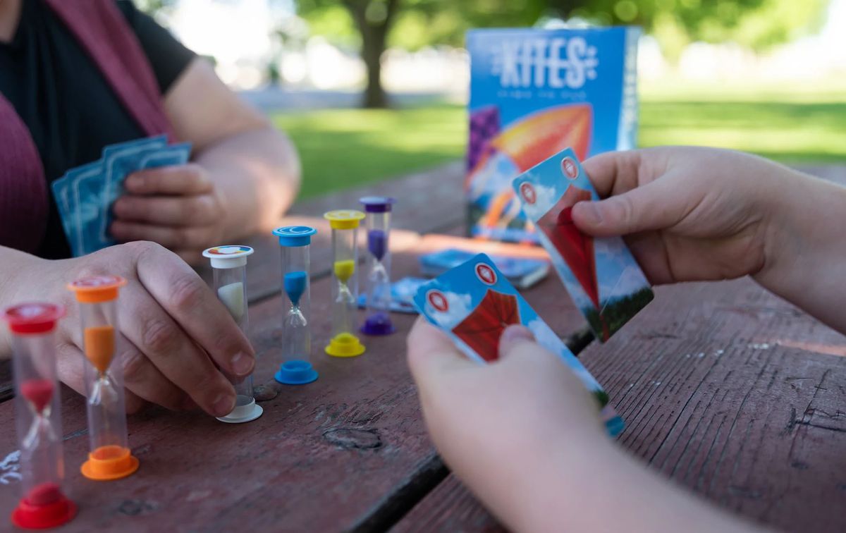 Los jugadores se sientan para un juego de cometas, con 5 relojes de arena entre ellos y una mano de cartas cada uno.