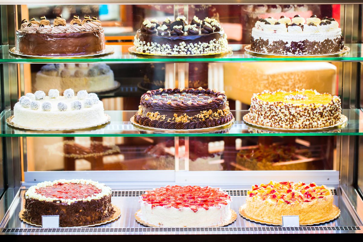 Nine cakes on three shelves in a glass display case