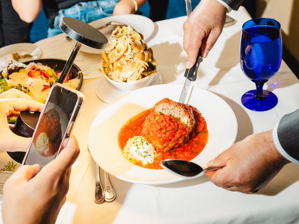 A meatball on a plate with people taking photos.