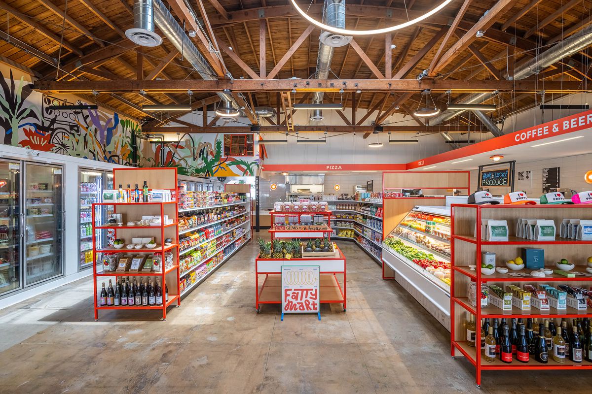 A tall warehouse with exposed ceiling and inside is several rows of high-end grocery, plus a frozen section.