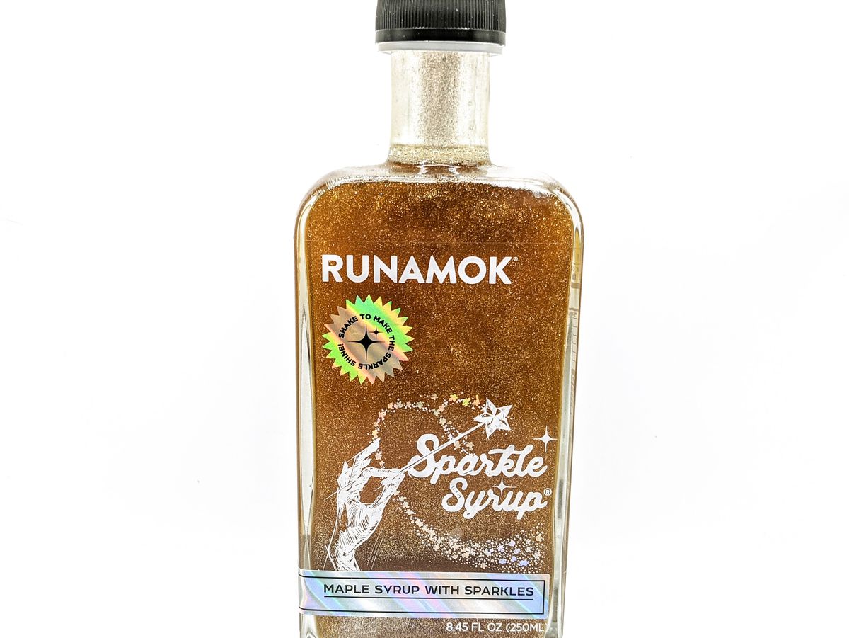 A glass bottle is full of a very glittery maple syrup. The label includes a hand waving a magic wand.