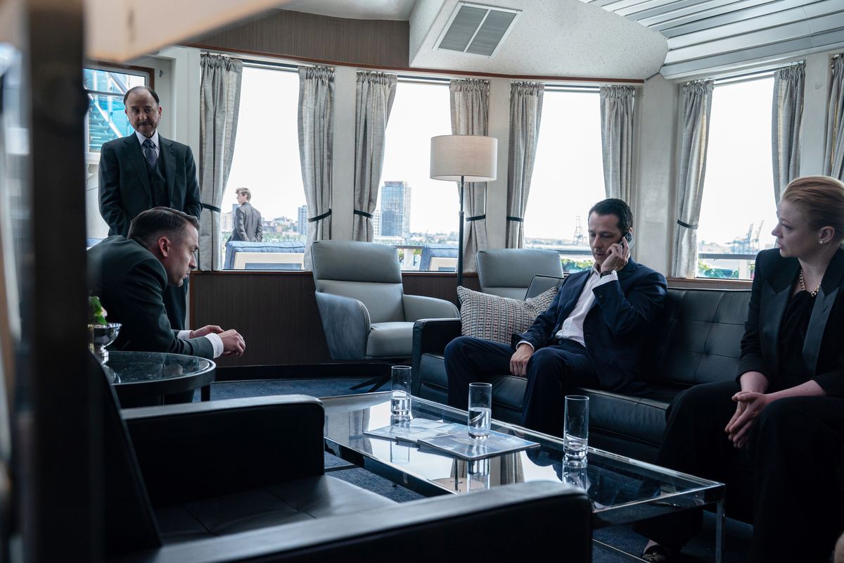 The Roy siblings sit around a glass coffee table while Kendall holds a phone to his hear in the fourth season of HBO’s Succession.