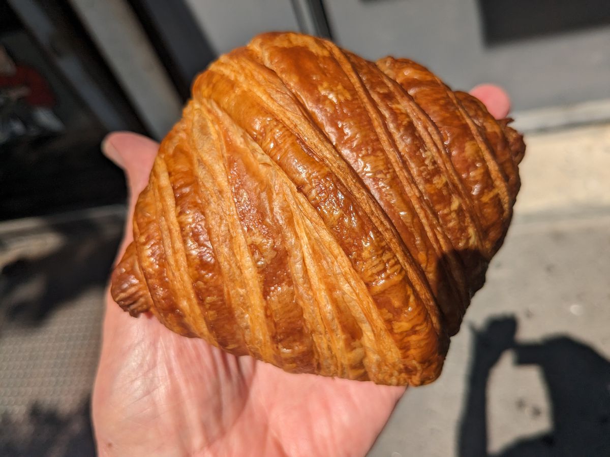 A hand holds a nearly rectangular croissant aloft.