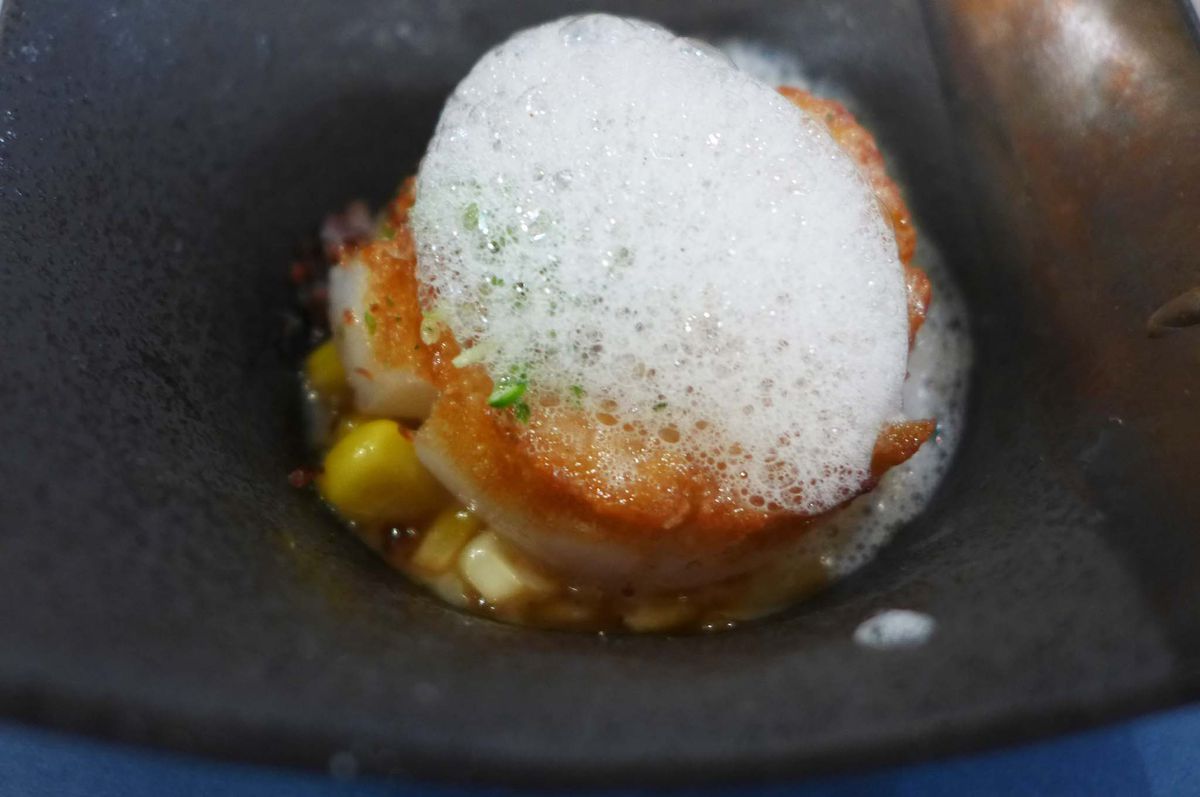 A square bowl with a scallop topped with foam.