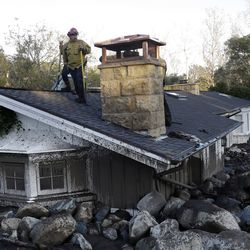 A firefighter stands on the roof of a house submerged in mud and rocks Wednesday, Jan. 10, 2018, in Montecito, Calif. Anxious family members awaited word on loved ones Wednesday as rescue crews searched grimy debris and ruins for more than a dozen people missing after mudslides in Southern California destroyed houses, swept cars to the beach and left more than a dozen victims dead. (AP Photo/Marcio Jose Sanchez)