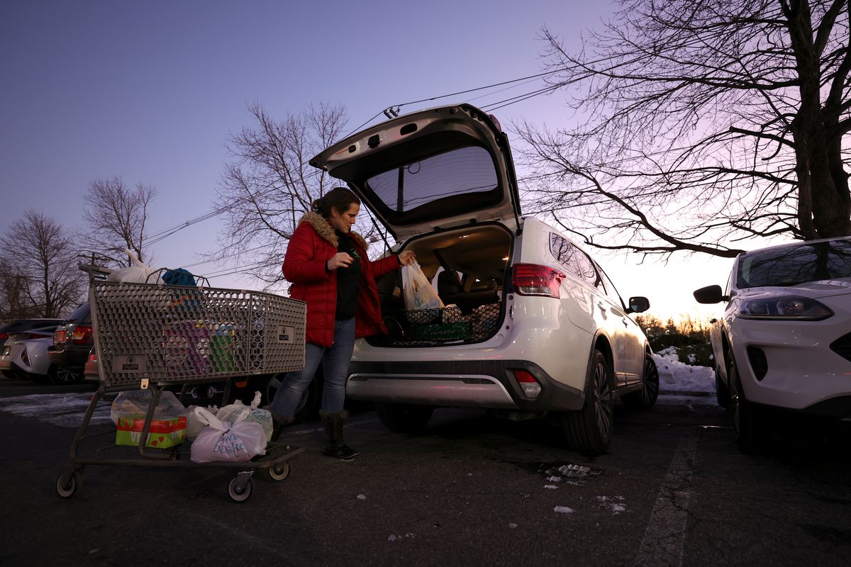 An Instacart worker loads groceries into the back of her car in an outdoor parking lot at twilight.