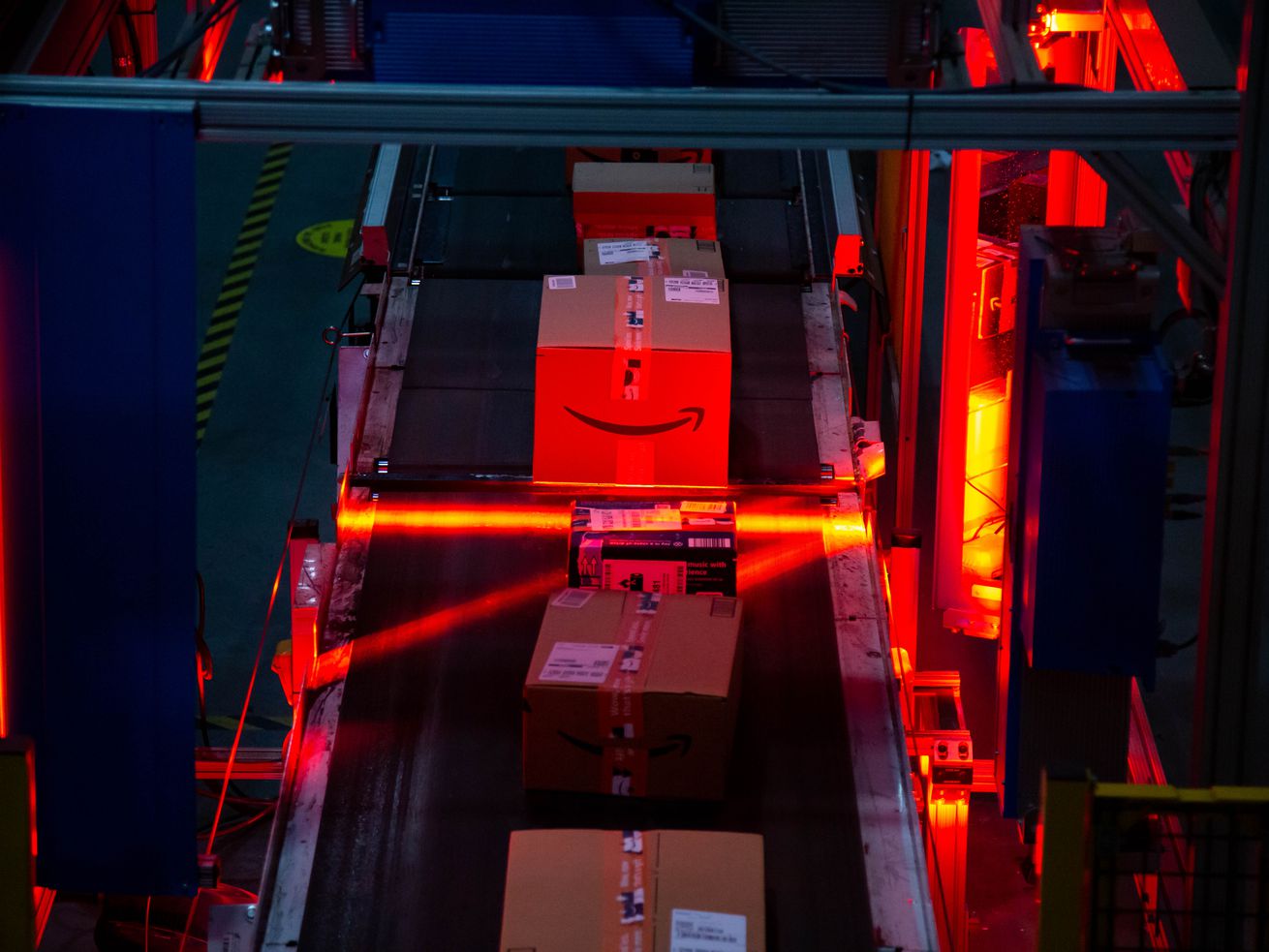 An Amazon-branded box moves through a red light scanner on a conveyer belt.