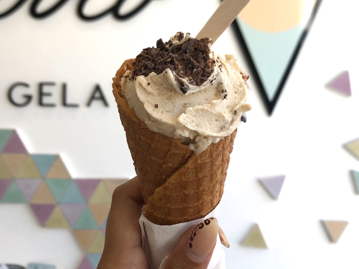 A woman’s manicured hand holding up an ice cream cone filled with hazelnut gelato.