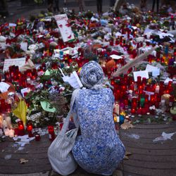 A woman sits next to candles and flowers placed on the ground after a terror attack that killed 14 people and wounded over 120 in Barcelona, Spain, Sunday, Aug. 20, 2017. (AP Photo/Emilio Morenatti)