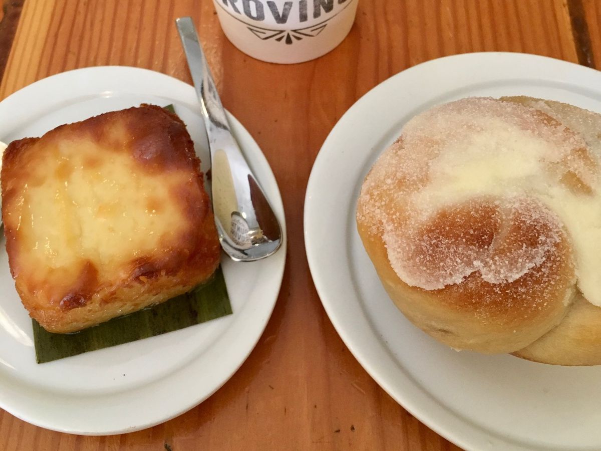 Two pastries sitting on two white plates side-by-side with a to-go coffee cup between them.
