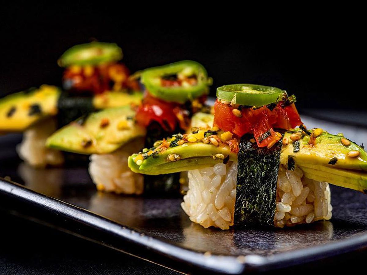 rice rolls topped with avocado and jalapeno against a black background