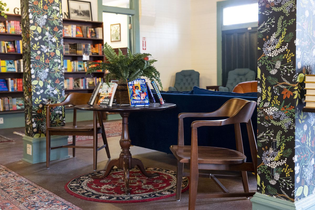 Installation d'une bibliothèque avec une table avec des livres et deux chaises en bois à côté de colonnes avec du papier peint à fleurs.