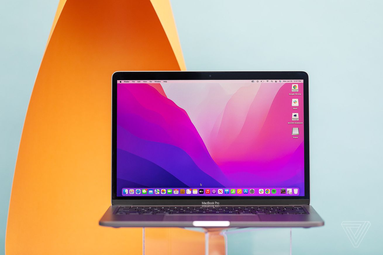 The MacBook Pro 13 2022 open on a transparent stand. The screen displays a pink and purple desktop background.