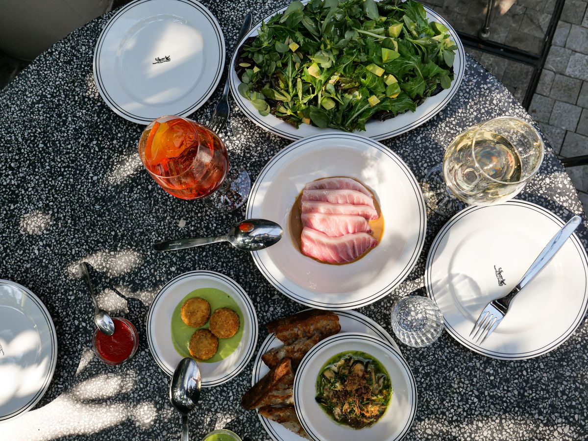 Dishes and cocktails on a dappled outdoor table.