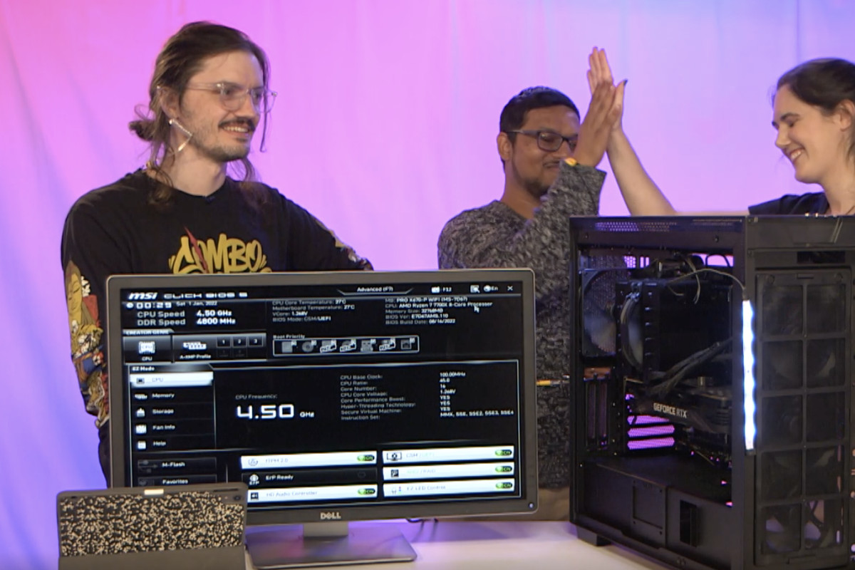 Polygon employees Simone de Rochefort and Samit Sarkar share a victorious high five as Patrick Gill looks on approvingly. They are standing behind a newly constructed PC with its side panels removed. A monitor on the table shows the PC’s BIOS screen, indicating that it is working— in theory.