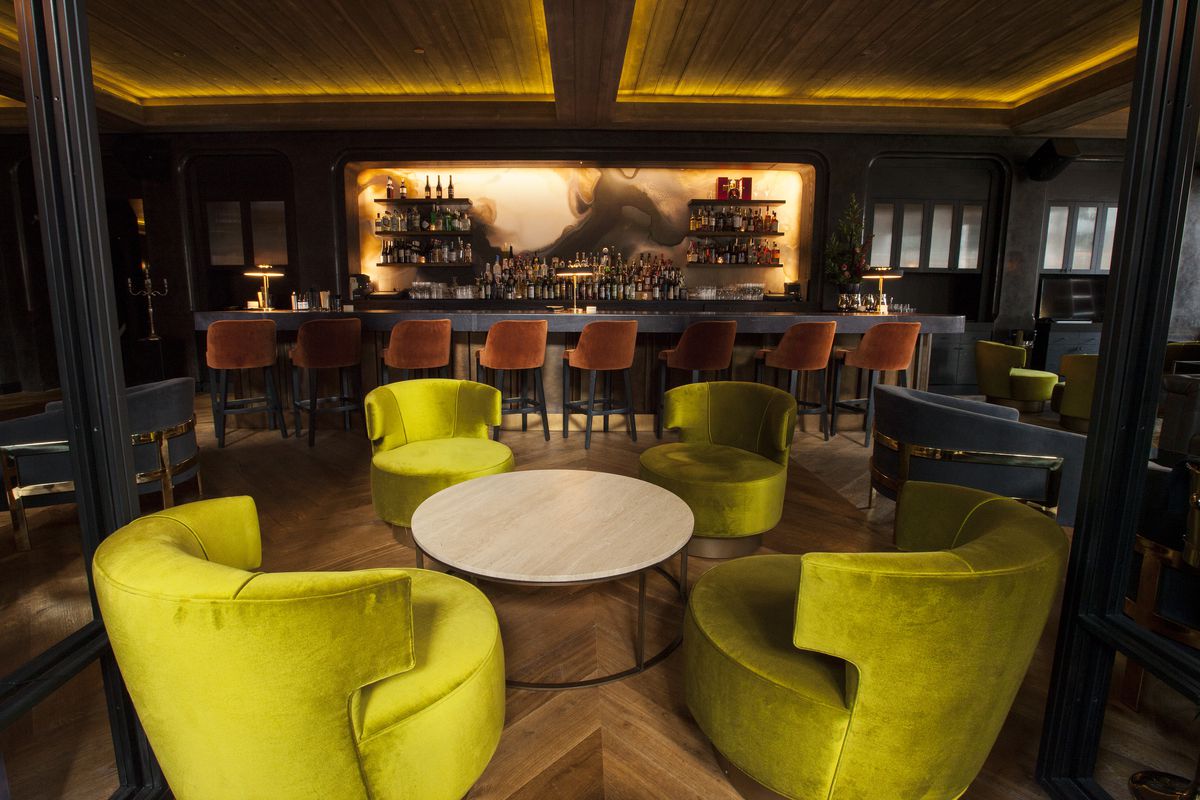 A moody bar space with green plush chairs.