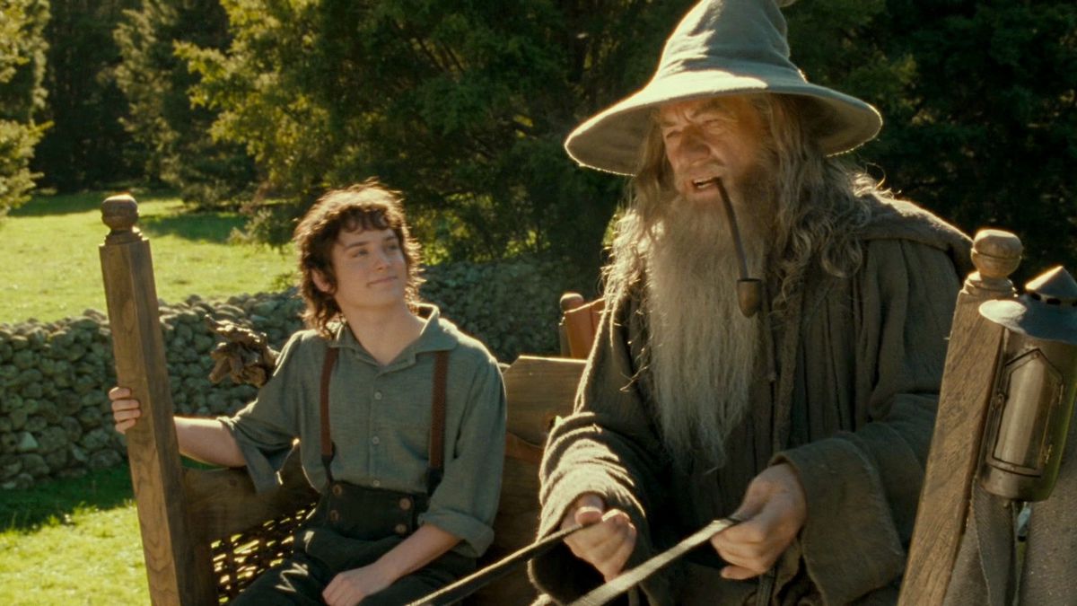 Frodo smiles like a goof while looking up at Gandalf who is steering the cart and smoking weed in The Lord of the Rings: Fellowship of the Rings