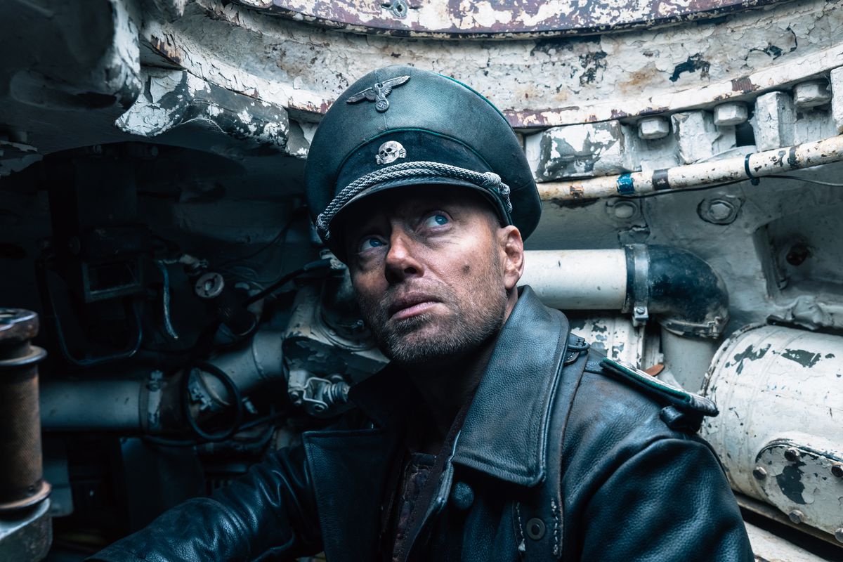 Aksel Hennie sits in a tank wearing his Nazi regalia in Sisu. He looks upwards towards the sky.
