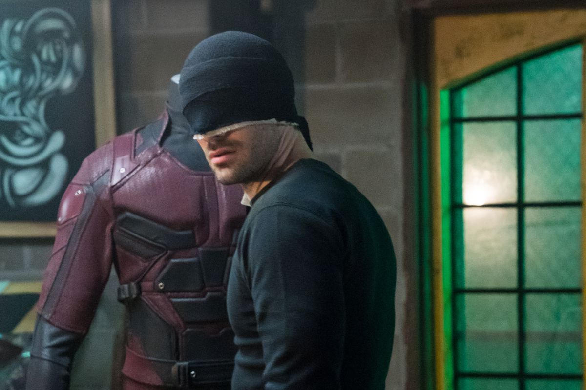 Daredevil (Charlie Cox) in his black ninja costume looking at the red daredevil costume from the 2015 Daredevil series.