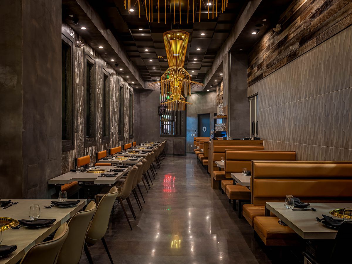 Wide view of ABSteak dining room with tan booths and lineup of tables with chairs.