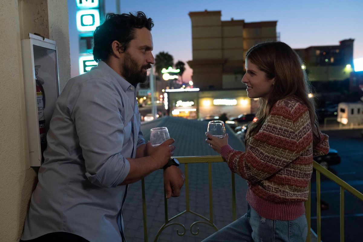 (L-R) Jake Johnson and Anna Kendrick standing on a balcony drinking out of stemless glasses in Self Reliance.