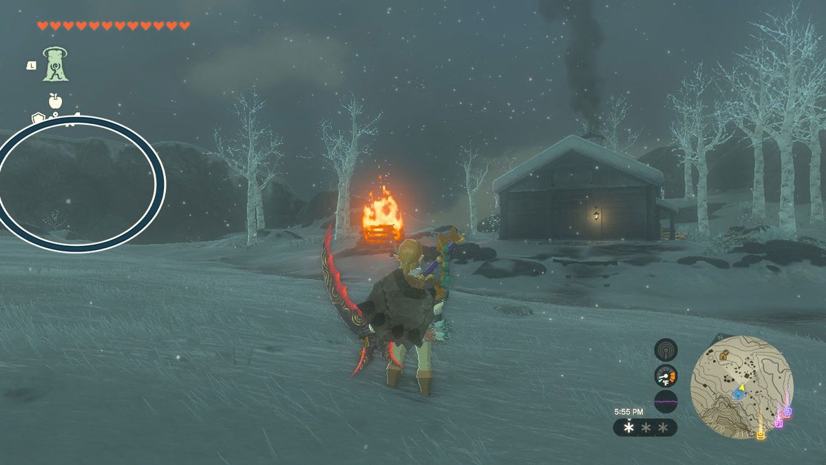 Link stands in front of a cabin on a snowy field. There is a bonfire to the left of the cabin. Even farther to the left is a cave entrance in a rock wall, and a circle is superimposed on the image so players can easily see it.