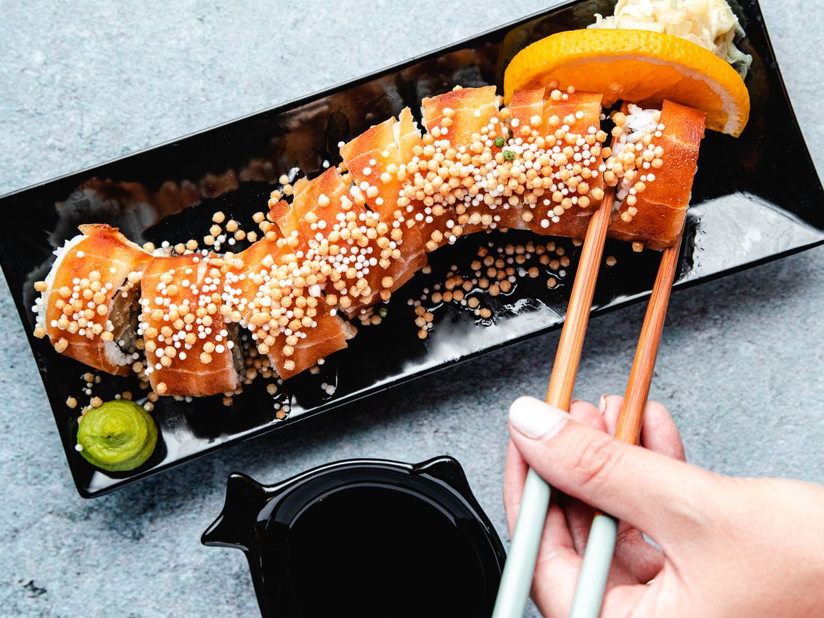 Wellness Sushi’s Smoky Sake Roll with chopsticks on a black dish.