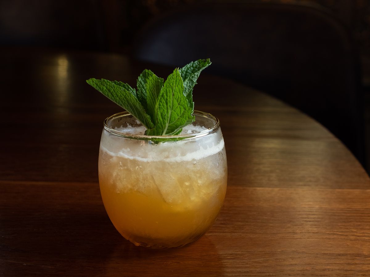 A lowball glass with a golden beverage is garnished with a bouquet of mint