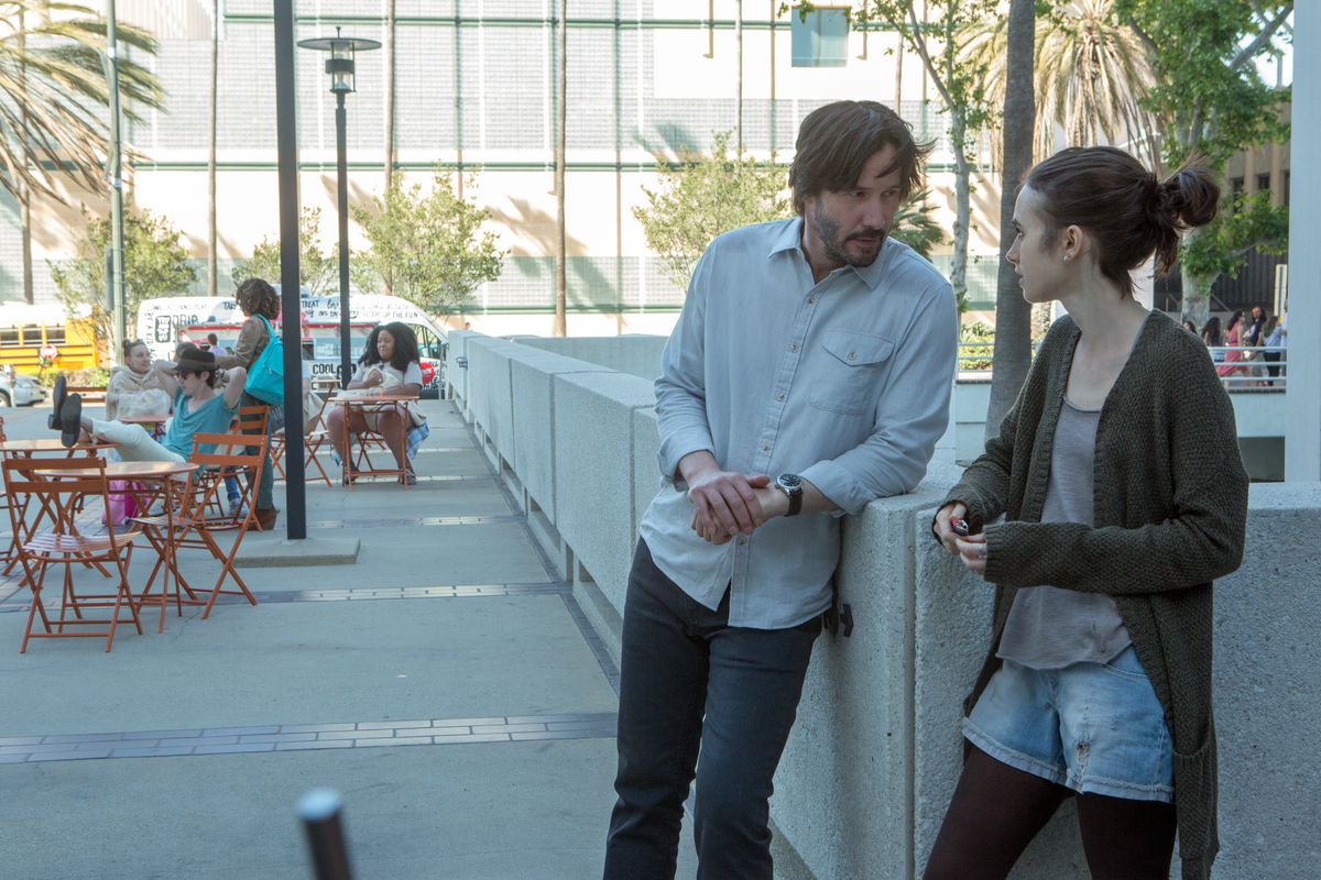 Keanu Reeves leans against an outside wall and talks to Lily Collins in To the Bone.