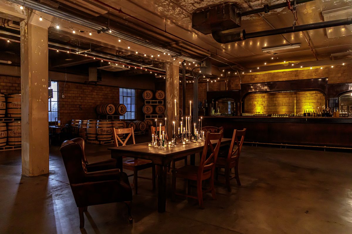 A table sits inside a dimly lit room with whiskey barrels, string lights, and candles.