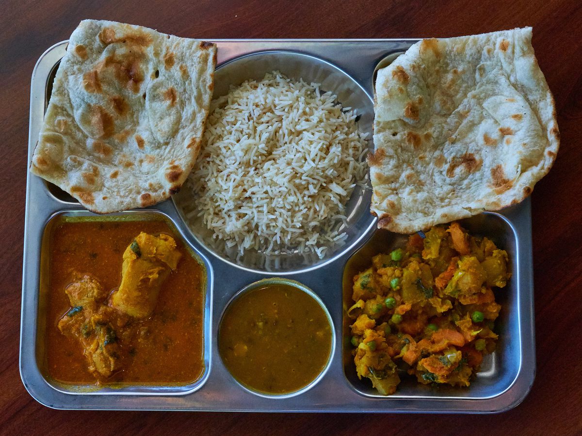 A metal tray filled with assorted curries and lentils, rice, and naan bread.