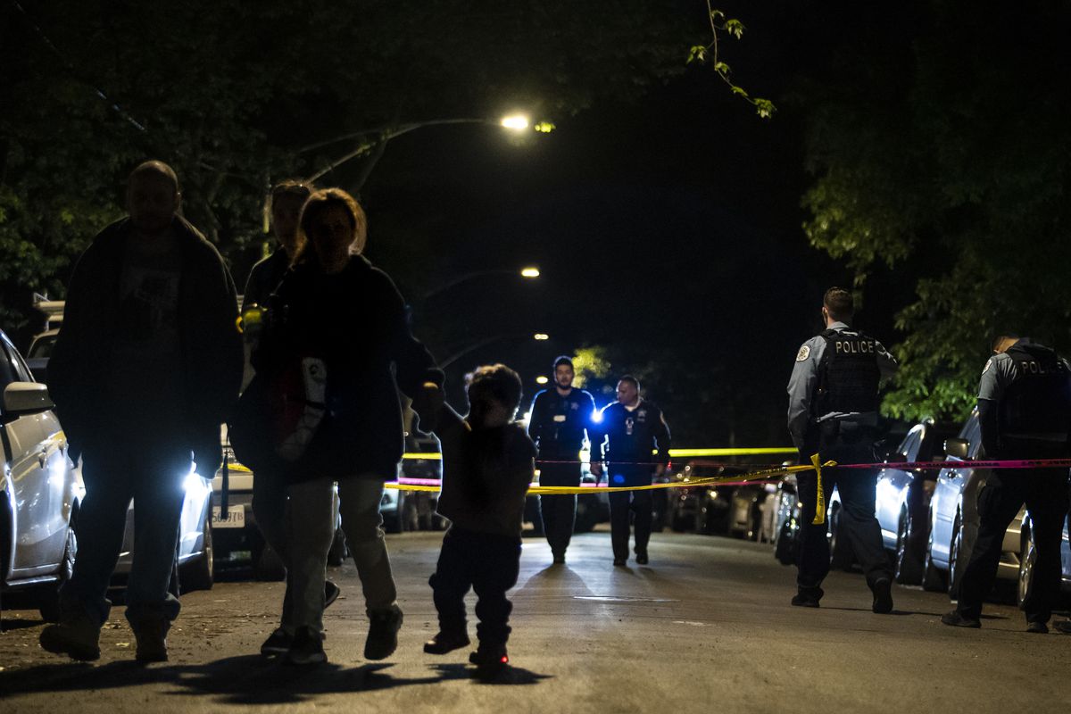 A family walks by as Chicago police investigate in the 3700 block of West McLean Avenue in Logan Square, where authorities said a 29-year-old man was shot multiple times Saturday night.