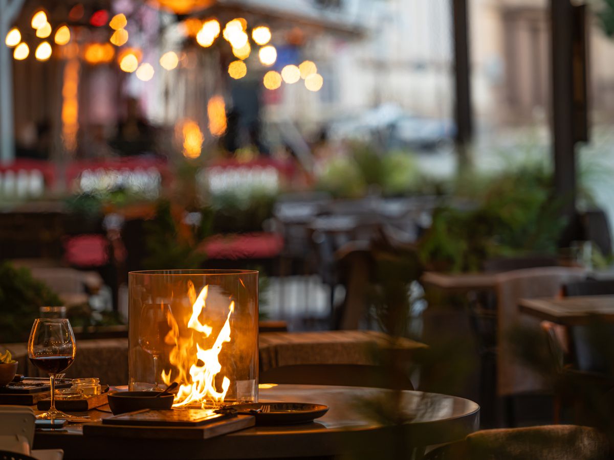 An enclosed firepit on an outdoor restaurant patio with a glass of wine visible alongside.