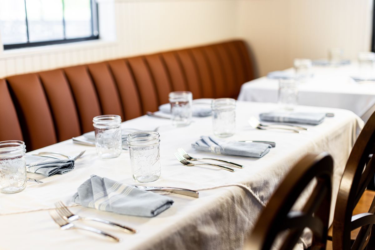 A close up of the dinner setting at Restaurant Beatrice, where white dishes sit on a white tablecloth with Ball jars for glasses.