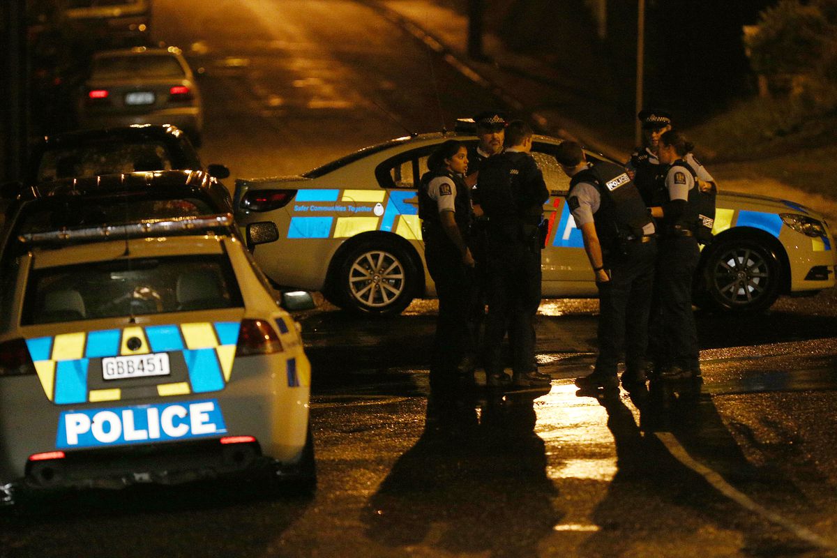 Police cars in Christchurch, New Zealand, are stopped on a street while the officers stand on the curb and talk.