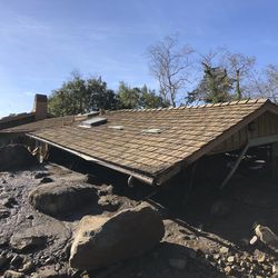 In this photo provided by Santa Barbara County Fire Department, mudflow, boulders, and debris from heavy rain runoff from early Tuesday reached the roof of a single story home in Montecito, Calif., on Wednesday, Jan. 10, 2018. A storm caused deadly mudslides in fire-scarred areas of Montecito and adjacent Santa Barbara County. (Mike Eliason/Santa Barbara County Fire Department via AP)
