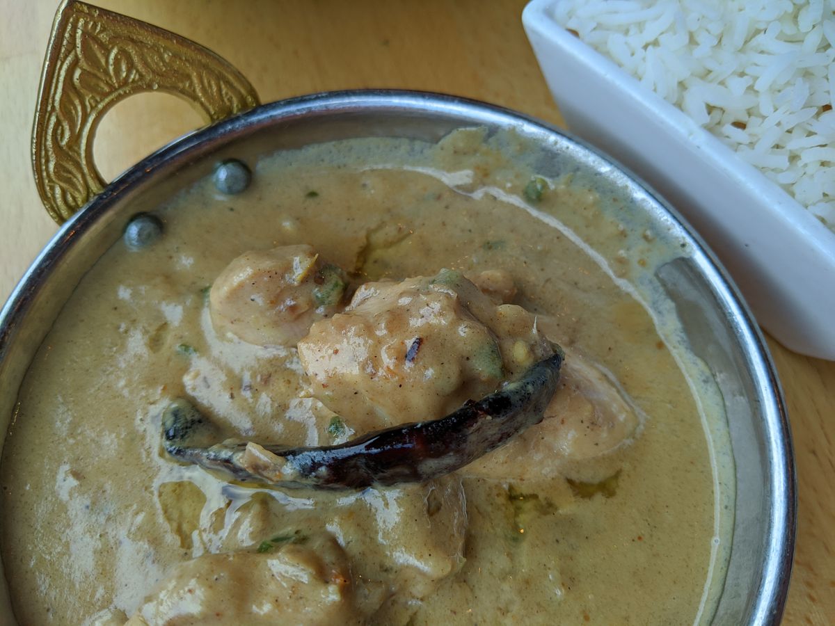 A bowl of curry with a dried chile pepper and light brown gravy.