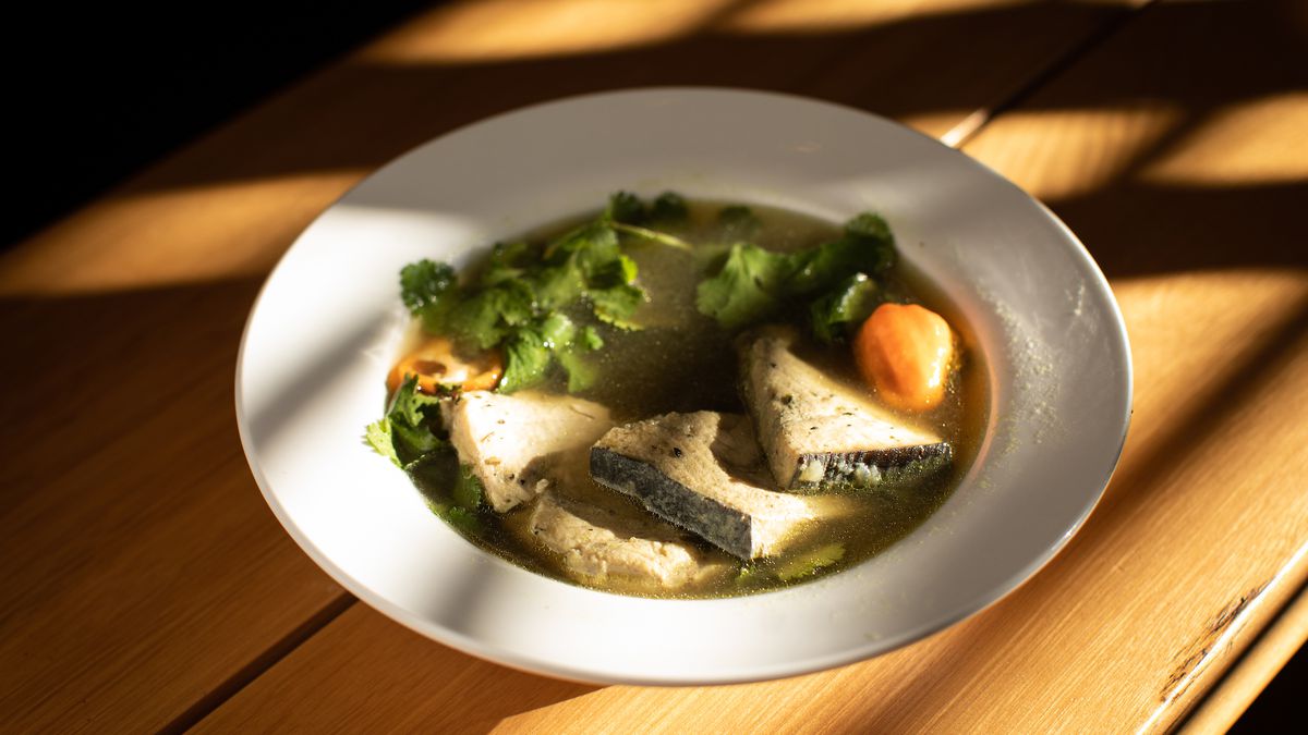Pepper soup sits in a white bowl with swordfish floating near the top.