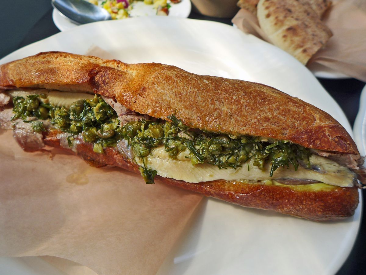 A long baguette with slices of tongue and green relish visible.