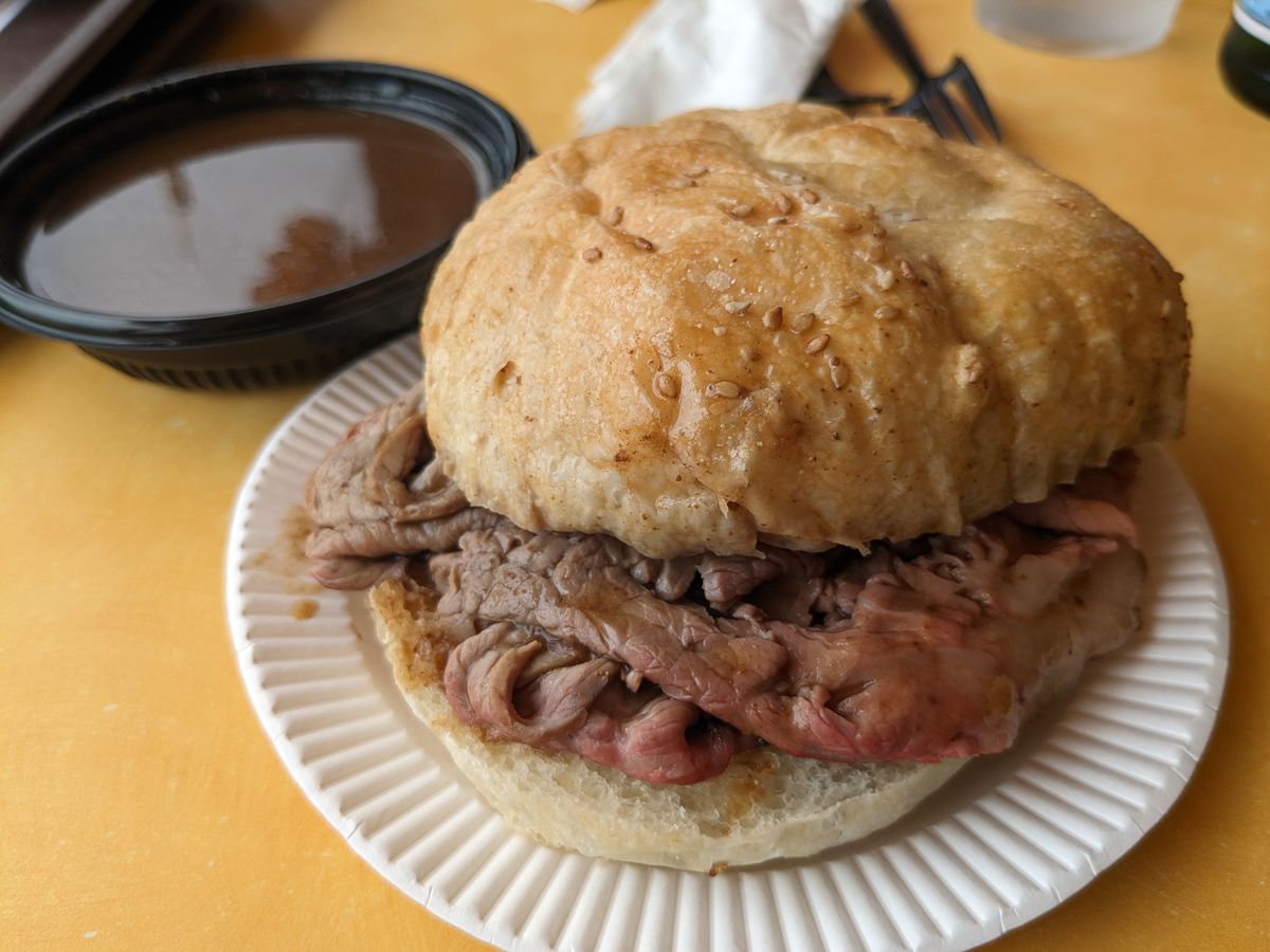 A round roast beef sandwich on a small paper plate.