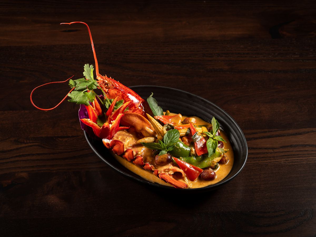 black bowl filled with lobster and bright curry sauce on a brown table