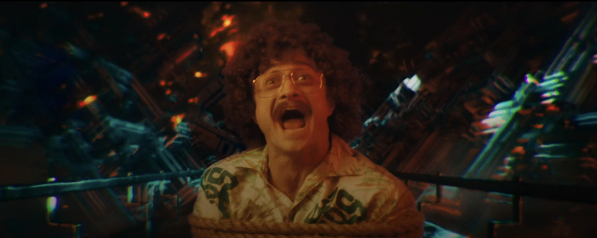 “Weird Al” Yankovic (Daniel Radcliffe), bound and stuck on a conveyer belt during an acid trip, stares into the camera and screams in Weird: The Al Yankovic Story
