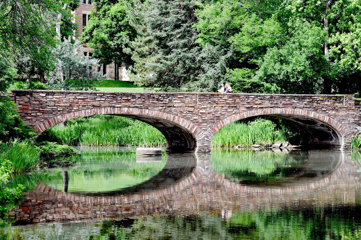 Two women cross the bridge over Varsity Pond on the University of Colorado Boulder campus on June 27, 2019.