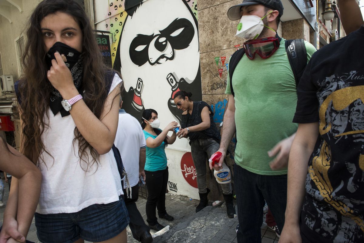 Masked protesters stand outside near a spray-painted wall.