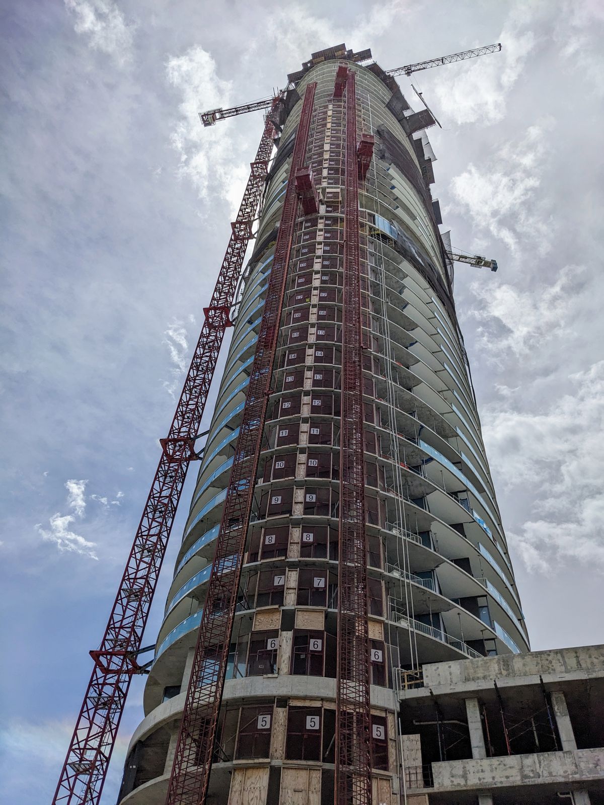 The Five Park tower under construction. It’s an oval-shaped tower with tall cranes and ladders on its sides.