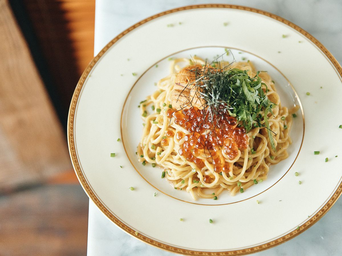 A gold and white plate with spaghetti pasta topped with uni and herbs.
