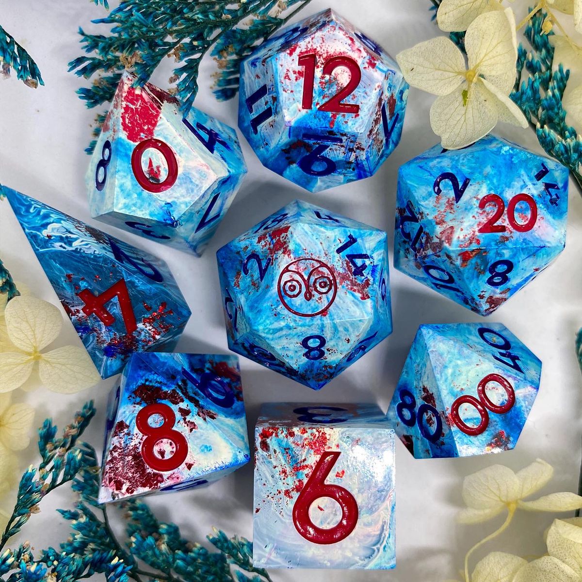 Blue and white dice with red, inked red, an owl logo on the 20-side.