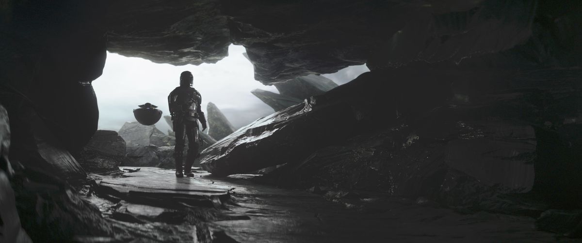 Mandalorian (Pedro Pascal) and Grogu walking into a cave. Grogu is in his hovering pod